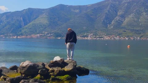 Man standing on small rock overlooking mountains and sea Stock Footage 237999008