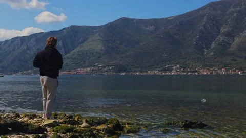 A man standing on a small rock throwing stones into the sea Stock Footage 237998290