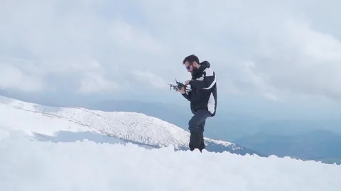 Man standing on snow covered mountaintop holding drone and controller. Video stock 249048096