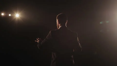 A man is standing on the stage and talking. He is waving his hands and talking Stock Footage 167895516