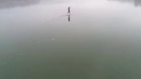 Man standing on stand up paddleboard on icy lake Stock Footage 127180010