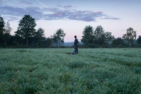 Man standing with stool and backpack in meadow at dawn. Noordijkerveld. Ach.. Foto stock