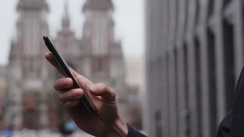 A man standing on the street is typing a message on his phone. Cropped view of Stock Footage 238909512