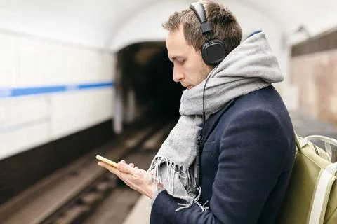 Man standing on the subway platform, looking at the screen of his mobile phone Stock Photos