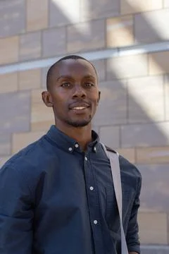 Man standing by tile facade with diagonal sun shadows, wearing navy shirt and Stock Photos