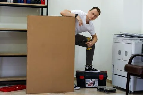 Man standing on tool chest drilling into large box in office Stock Photos
