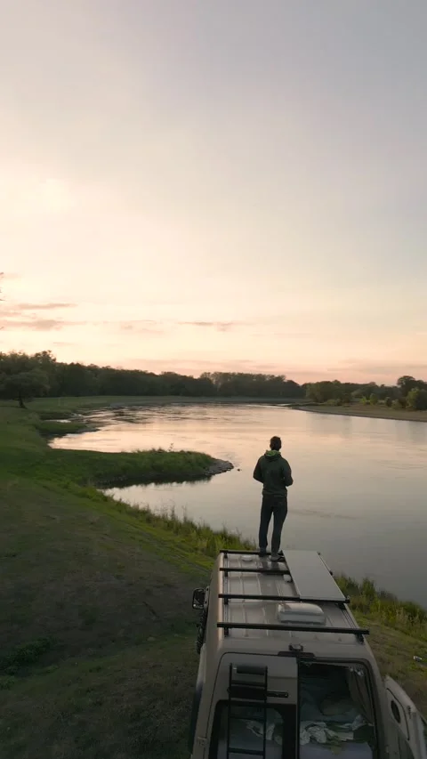 Man standing on top of a camper van enjoying the view over a river Video stock 226206430