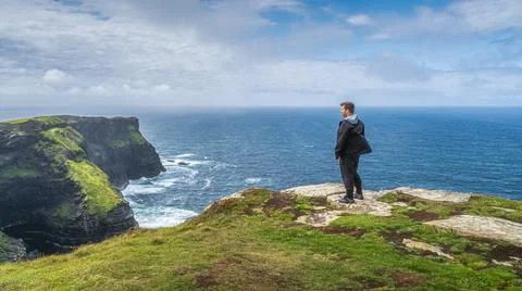 Man standing on the top of iconic Cliffs of Moher and admiring spectacular vi Stock Photos