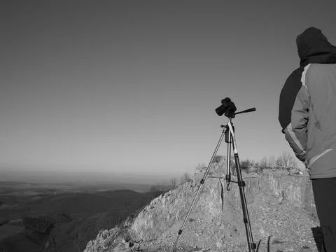Man standing with a tripod and camera on the edge of a rocky mountain. Stock Photos