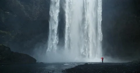 Man standing under majestic Skogafoss waterfall Stock Footage