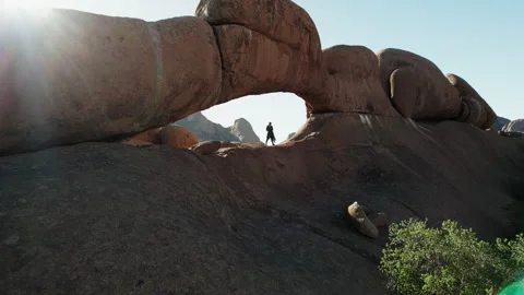 Man standing under rock arch in African desert landscape Stock Footage 315958267
