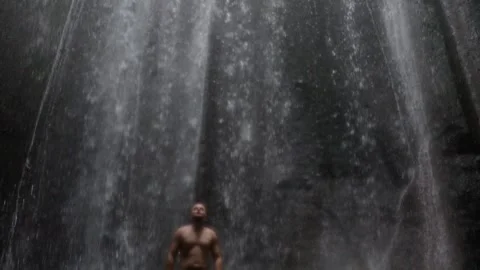 Man standing under waterfall feeling freedom and serenity Stock Footage 340848294