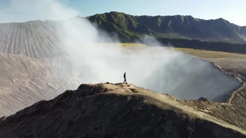 Man Standing at Volcano Edge – Drone Pullback Reveal 4K Stock Footage 315117959