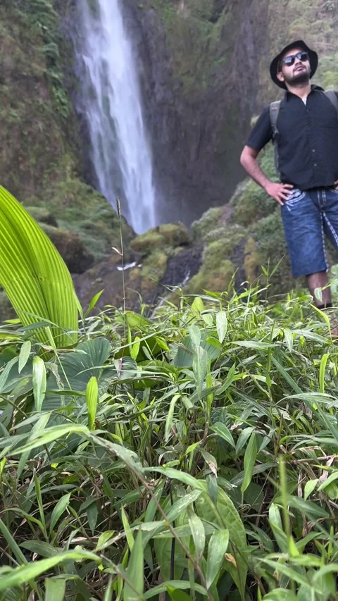 Man Standing by Waterfall on Dirt Path in Tropical Forest Vertical Video stock 323908514