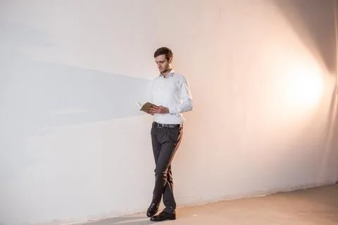 A man standing by the white wall, reading a book Stock Photos