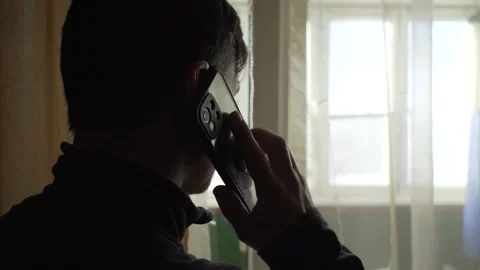 A man is standing at the window and talking on a mobile phone. Close-up Stock Footage 242119739