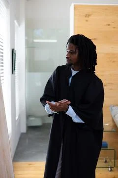 Man standing by window with blinds in modern flat wearing ceremonial gown, Stock Photos