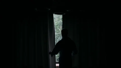 A man standing by the window opens the curtains, frame in backlight Stock Footage 270963838