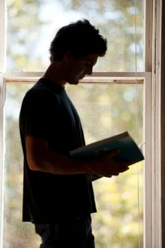 Man standing at window reading Foto stock