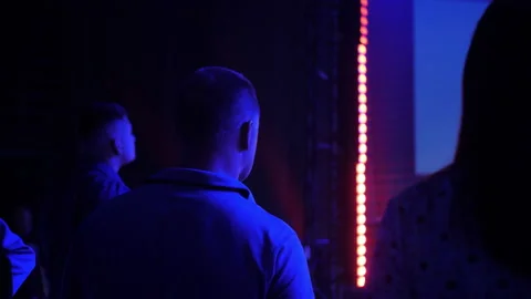 A man stands against the backdrop of a large stage in darkness. Stock Footage 219849138