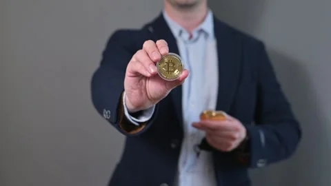 A man stands against a gray background holding a coin in one hand and a small Stockbeeldmateriaal 338300063