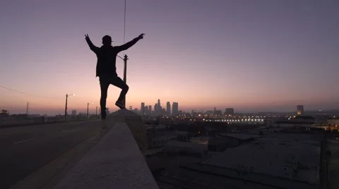 Man Stands with Arms Raised While Sun Sets Over Los Angeles City Stock Footage 56100807