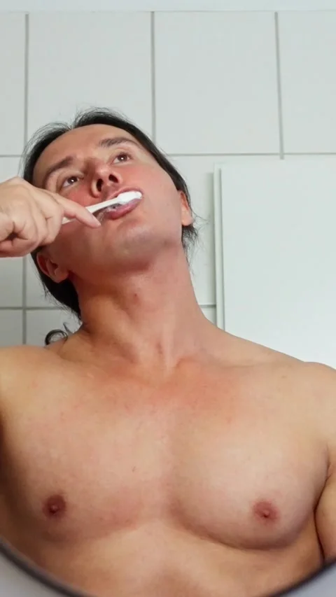 A man stands in a bathroom, brushing his teeth and focusing on personal hygiene Stock Footage 312476056