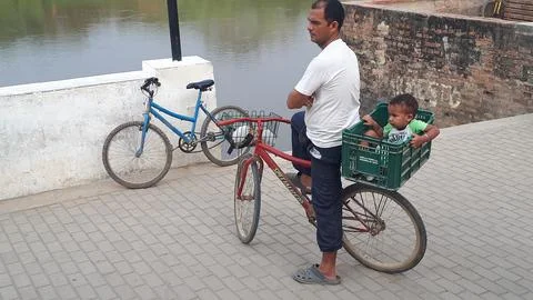 Man stands beside a bicycle while a small child sits in a crate mounted on the Stock Photos