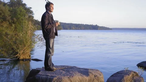 A Man Stands on the Big Stone Lying in the River with a Cup of Tea in the Hand Stock Footage 97600089