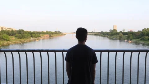 A man stands on a bridge overlooking the Danube River at sunset. Stock Footage 319763012