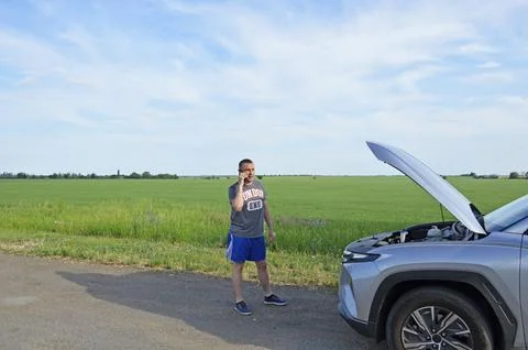 Man stands by a broken down car,makes a phone call and looks under the open hood Stock Photos