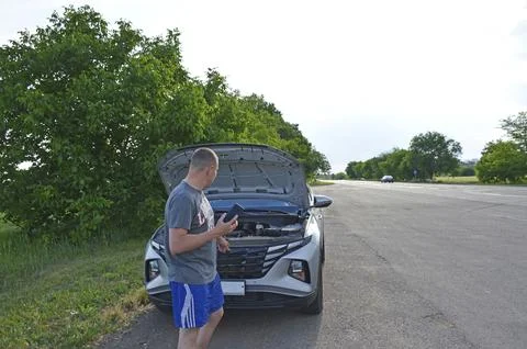 Man stands by a broken down car,makes a phone call and looks under the open hood Stock Photos