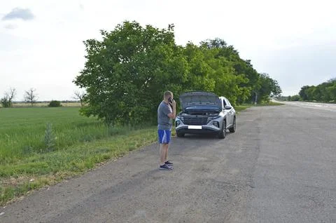 Man stands by a broken down car,makes a phone call and looks under the open hood Stock Photos