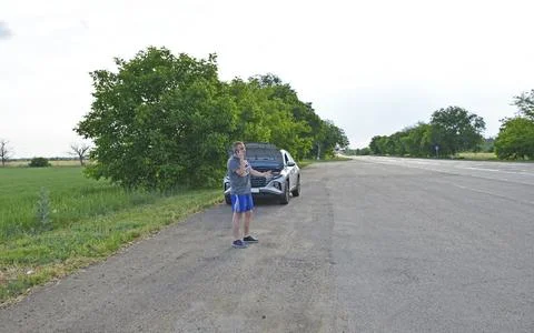 Man stands by a broken down car,makes a phone call and looks under the open hood Stock Photos