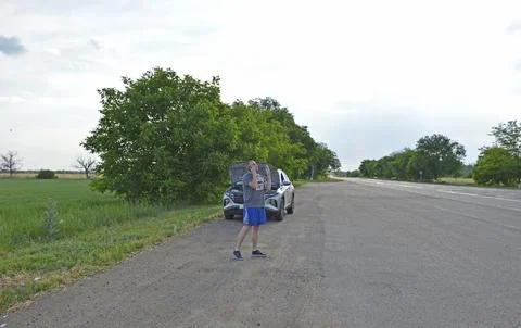 Man stands by a broken down car,makes a phone call and looks under the open hood Stock Photos