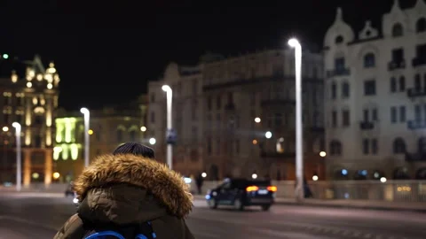 A man stands at a bus stop at night. blurred night city background Stock Footage 234429637
