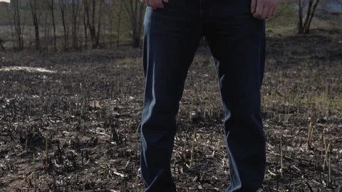 A man stands on a charred field after a fire. A person s face is not visible. Stock Footage 130725980