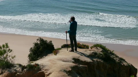 Man Stands on a Cliff Above the Ocean and Drinking Water from Bottle Stock Footage 46495293