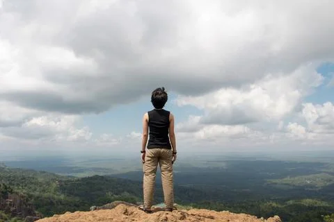 A man stands on a cliff facing back and looking at the nature and clouds. Stock Photos
