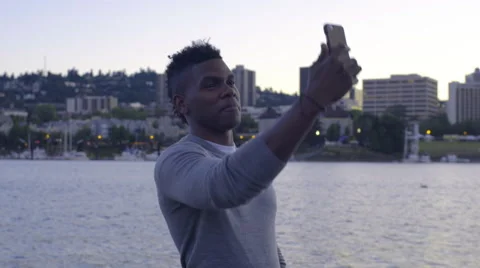 Man Stands On A Dock And Takes Selfies, Beautiful View Of City In Background Stock Footage