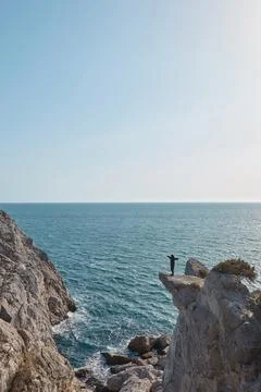 A man stands on the edge of a cliff, hands spread out in different directions Stock Photos