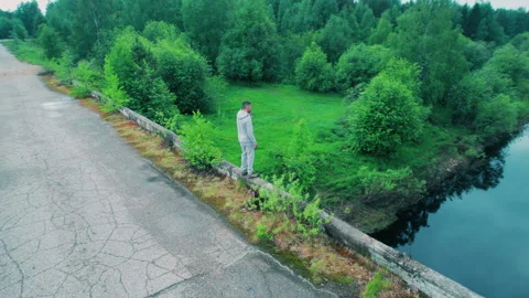 A man stands on the edge of an old bridge without a guardrail and looks down. Stock Footage 310856920