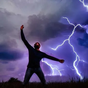 A man stands in a flash of lightning with his hands raised to the sky. Field  스톡 사진