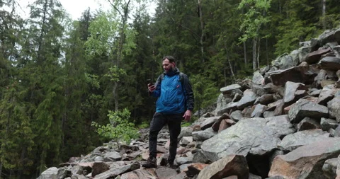 A man stands in the forest on large stones and takes out a smartphone Stock Footage 243598709