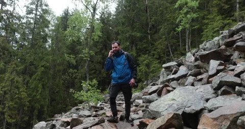 A man stands in the forest on large stones and takes out a smartphone Stock Footage 243599256