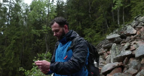 A man stands in the forest on large stones and takes out a smartphone Stock Footage 243600169