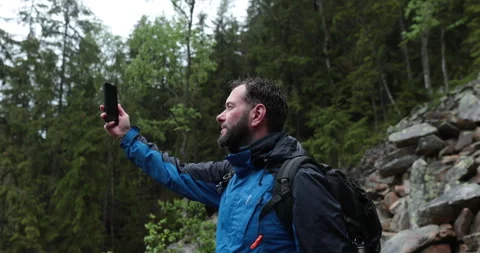 A man stands in the forest on large stones and takes out a smartphone Stock Footage 243600395