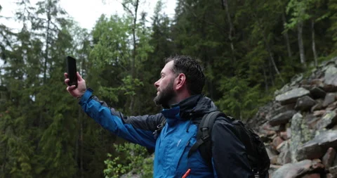 A man stands in the forest on large stones and takes out a smartphone Video stock 243600563