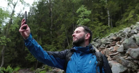 A man stands in the forest on large stones and takes out a smartphone Video stock 243603146