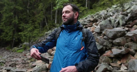 A man stands in the forest on large stones and takes out a smartphone Video stock 243603392